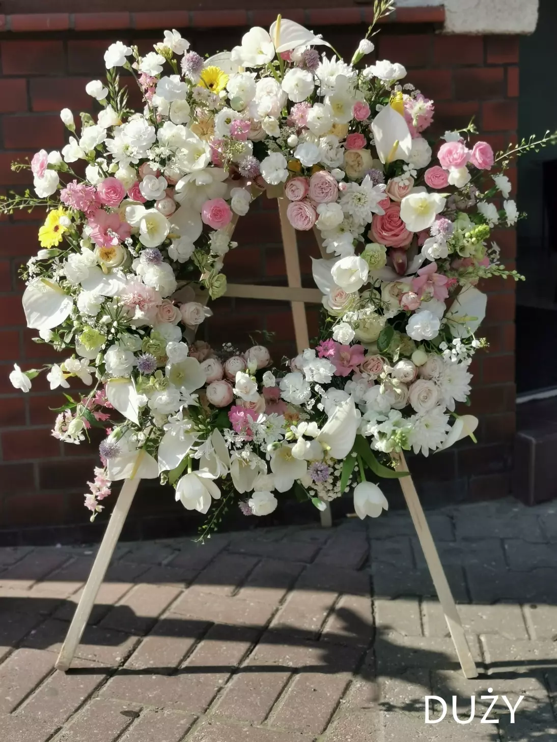 The wreath consists of harmoniously selected species of flowers, subdued colours, including: English roses, twig and full roses, anthurium flowers, gerberas, carnations, ferns, tulips, agapanthus, garlands, eustoma.