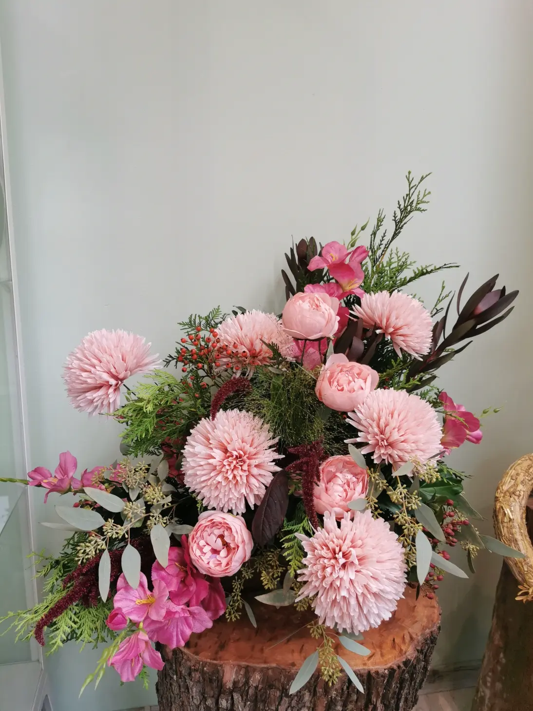 Forma przestrzennej i okazałej dekoracji wykonanej z kwiatów sztucznych: pudrowo- różowych chryzantem igiełkowych, róż, mieczyków oraz naturalnych.